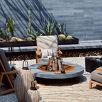 Outdoor patio furniture arrangement featuring a round stone fire pit with logs, wooden lounge chairs, a gray armchair, and decorative lanterns in front of a dark slate wall with potted cacti.