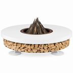 A round outdoor fire pit table with a white top, a wood-burning insert with a pile of branches, a base filled with stacked firewood, and small white pedestal legs, shown on a plain white background.